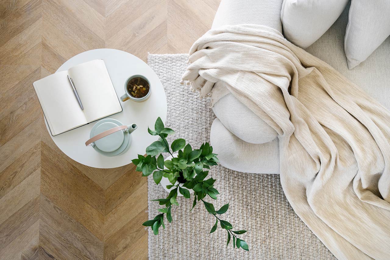 Overhead view of an open book, plant, tea and couch in living room interior design