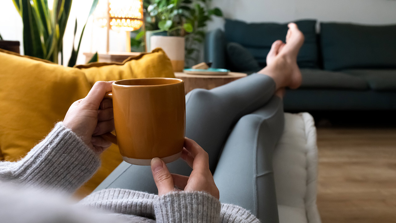 POV of young woman relaxing at home with cup of coffee lying on couch
