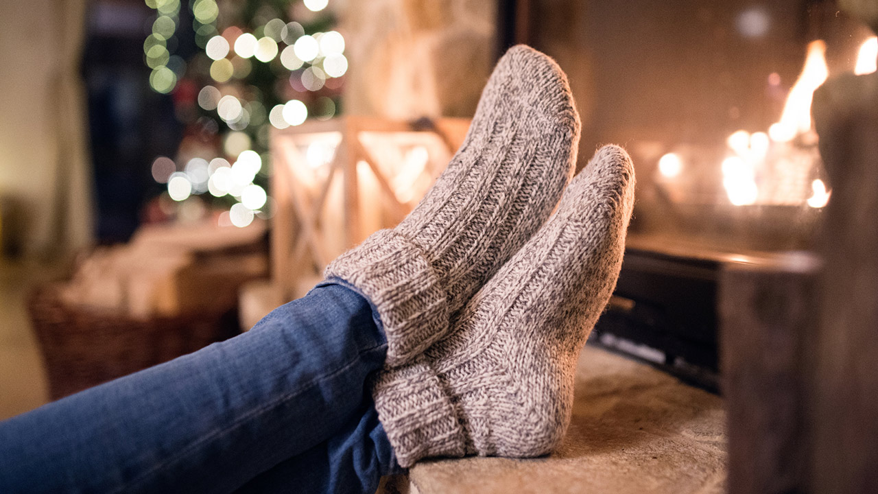 Feet of unrecognizable woman in woollen socks by the Christmas fireplace