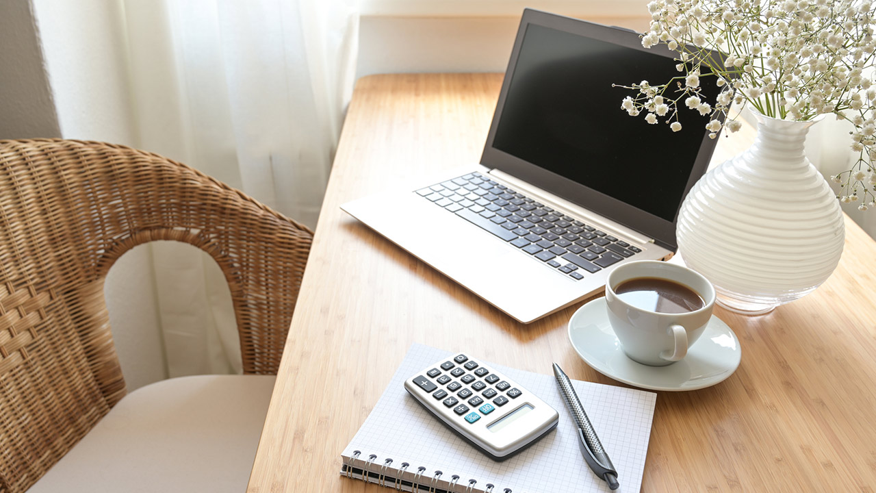 Home office desk with laptop computer, calculator, spiral book, coffee and a white flower bouquet, business accounting concept, copy space, selected focus