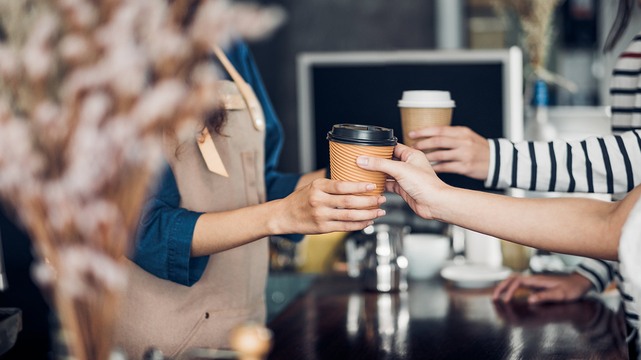 Barista served take away hot coffee cup to customer at counter bar in cafe restaurant