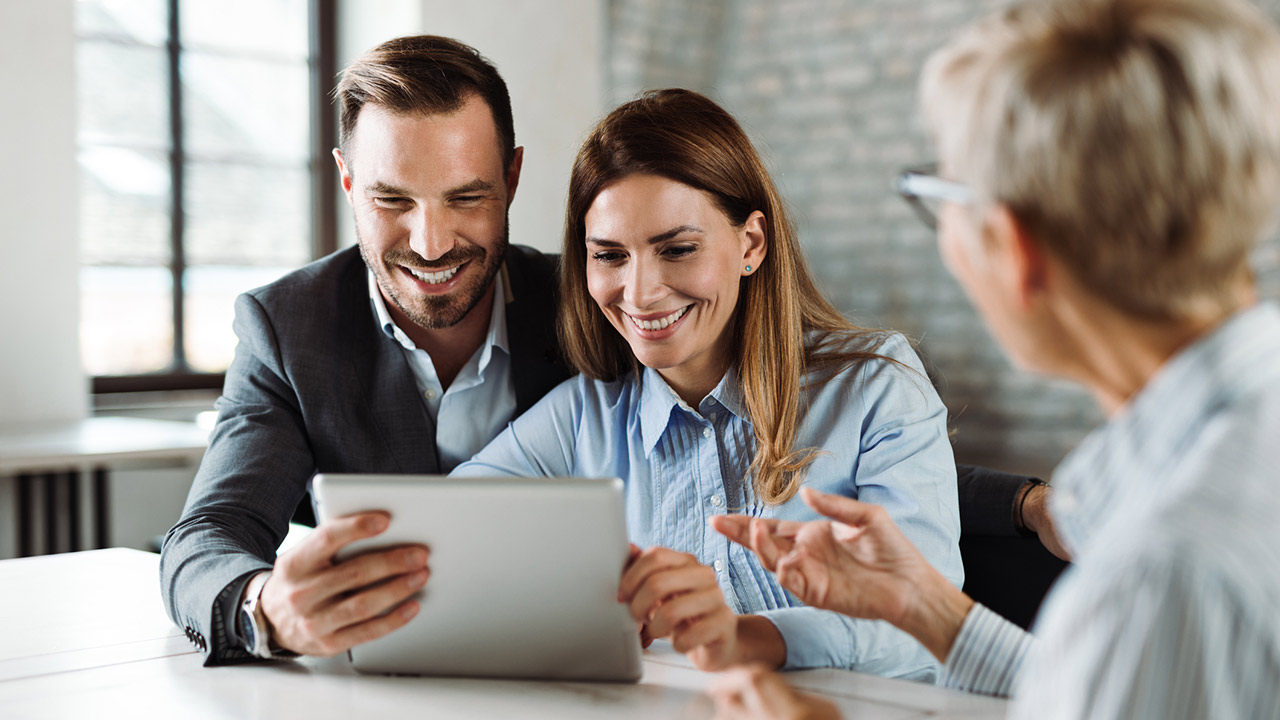 Happy couple using tablet while having a meeting with their real estate agent in the office