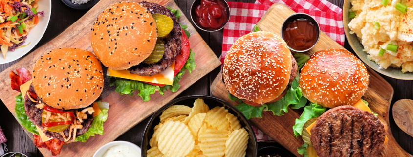BBQ table scene with hamburgers, classic salads and snacks over dark wood stock photo
